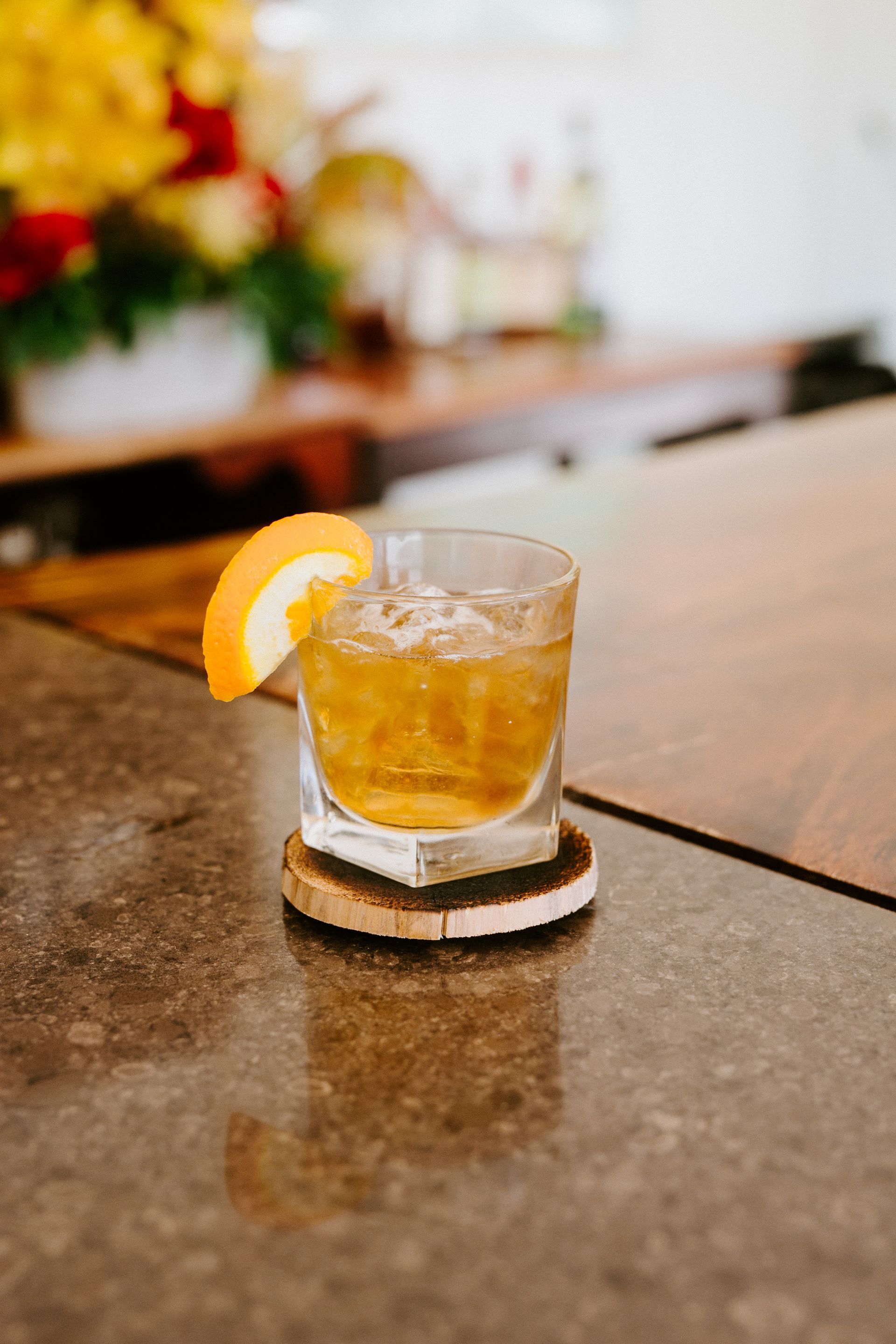 Cocktail in a glass with orange slice garnish, on a coaster, on a bar.