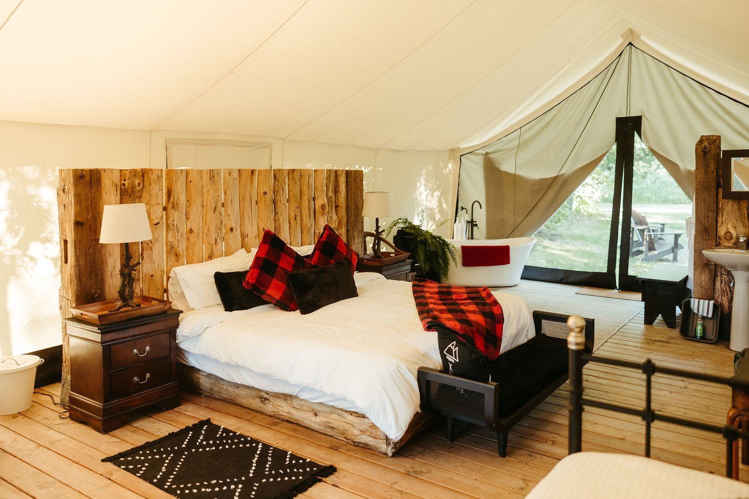 Interior of a glamping tent with a bed, wood headboard, bedside table, and open tent flap.
