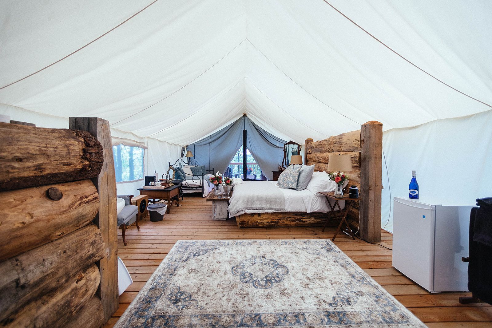 Glamping tent interior with bed, rug, and rustic wooden beams.