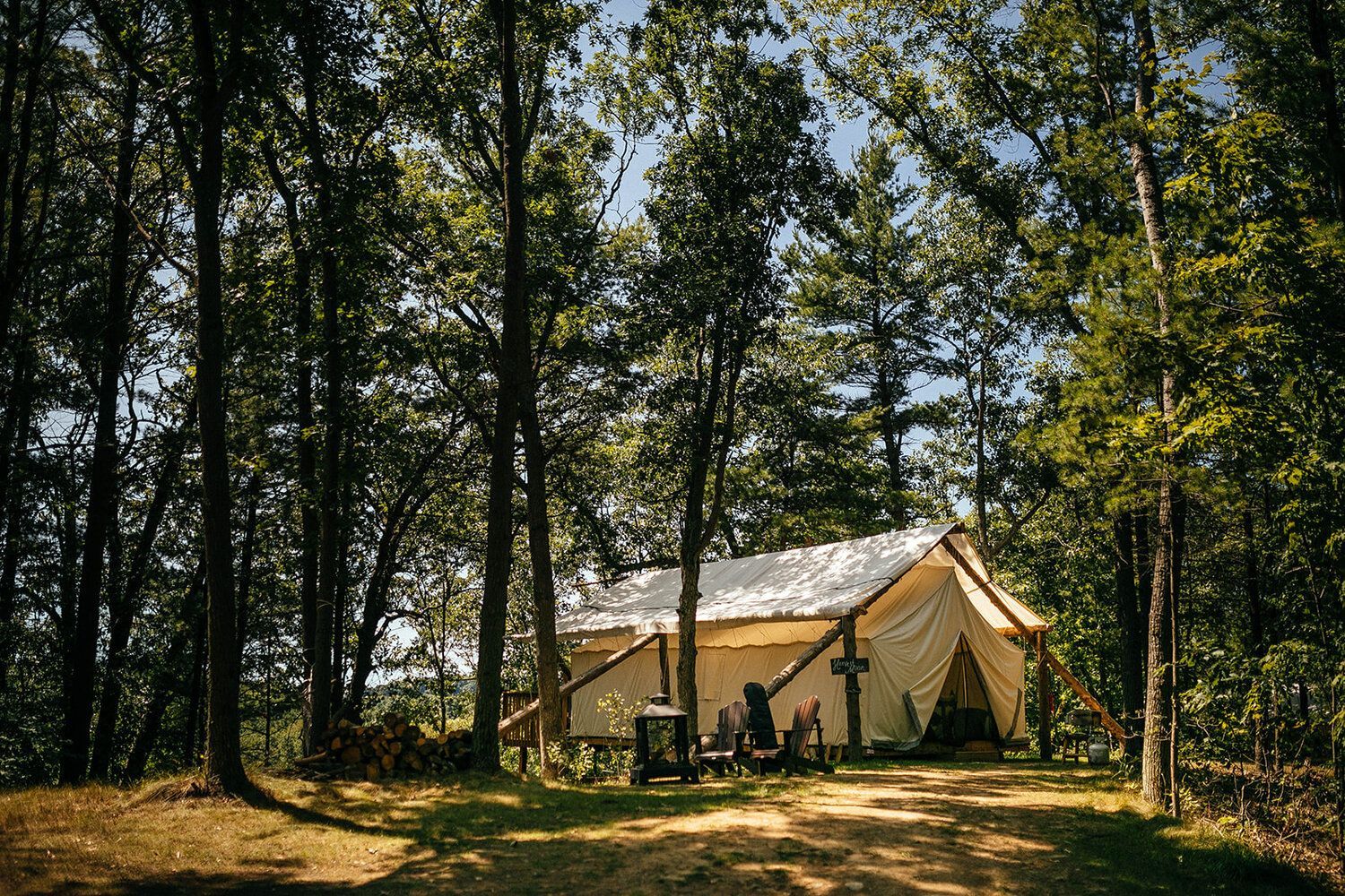 Canvas tent nestled in a forest, sunlight filtering through trees.