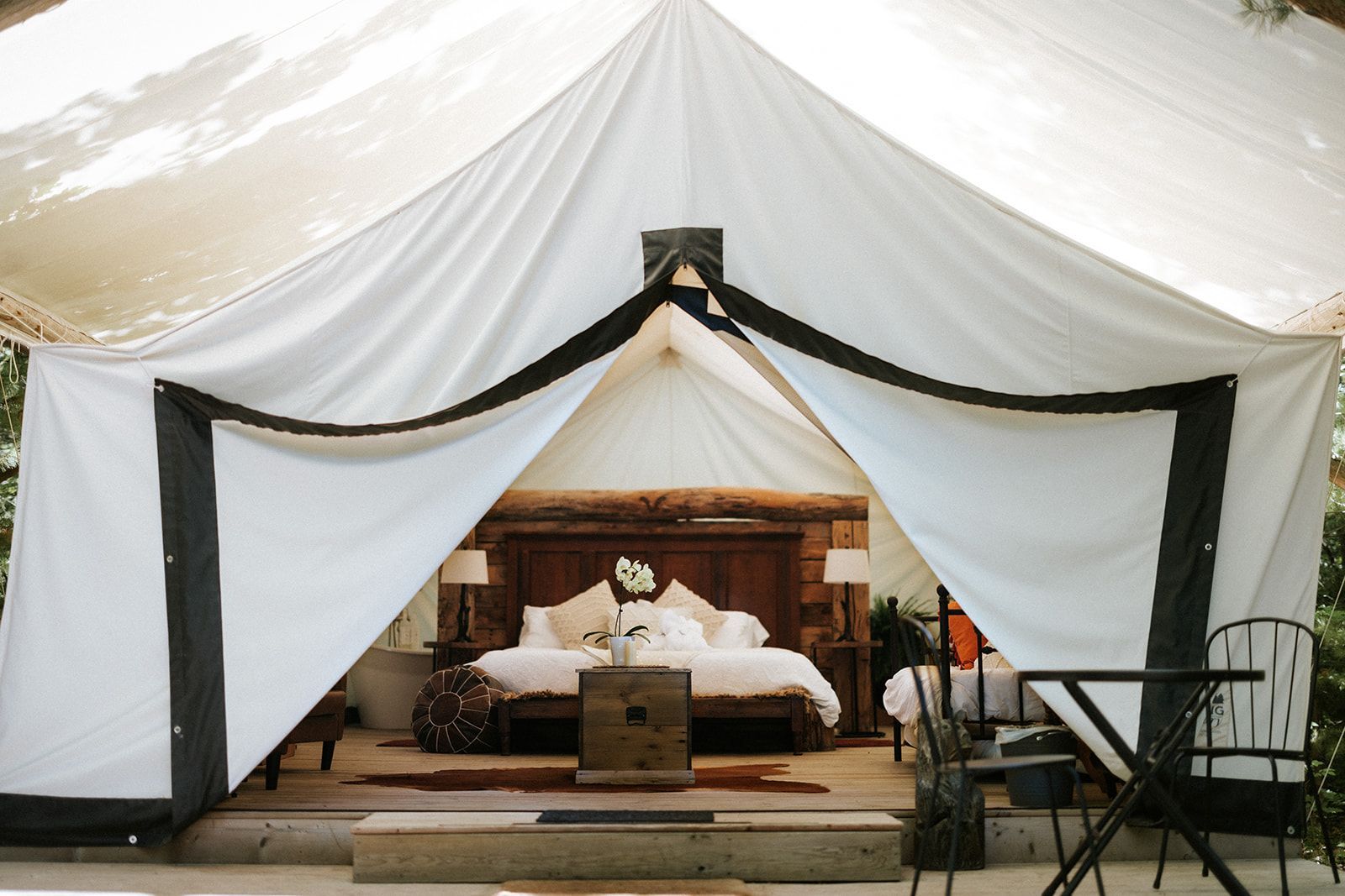 White canvas glamping tent entrance reveals a furnished bedroom with bed, lamps, and a small table.