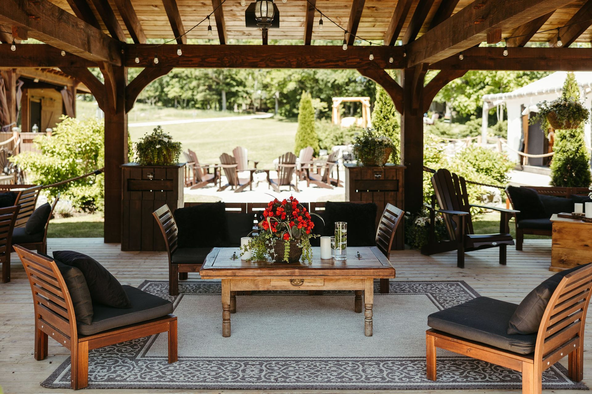 Patio with wooden furniture, a rug, and a rustic coffee table, under a wooden pergola, overlooking a lawn.