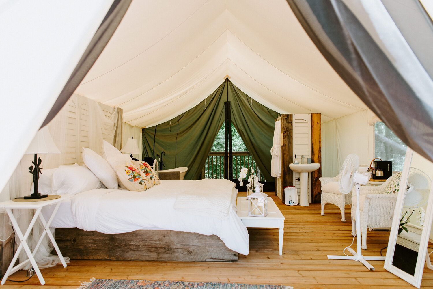 Interior of a luxurious glamping tent with white bed, furnishings, and wooden floor.