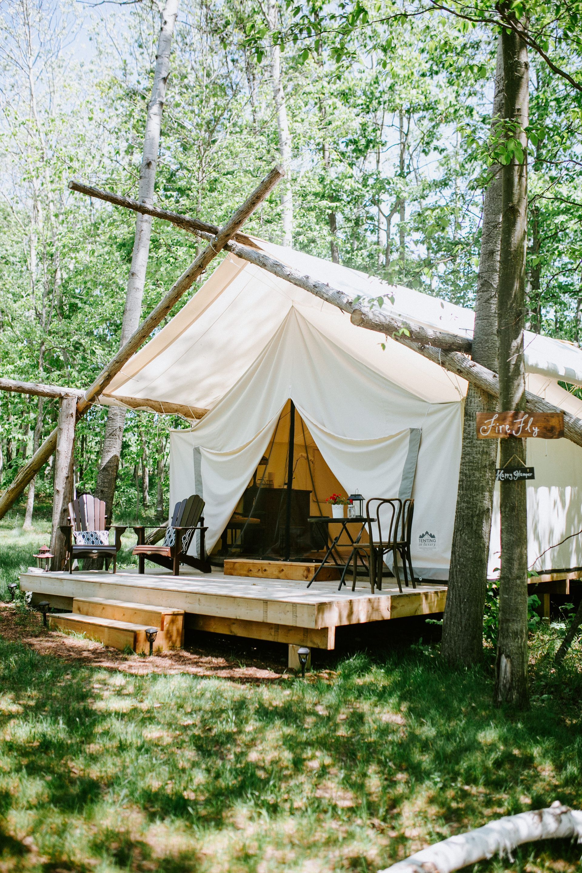 Canvas tent with wooden deck and furniture in a forest clearing.