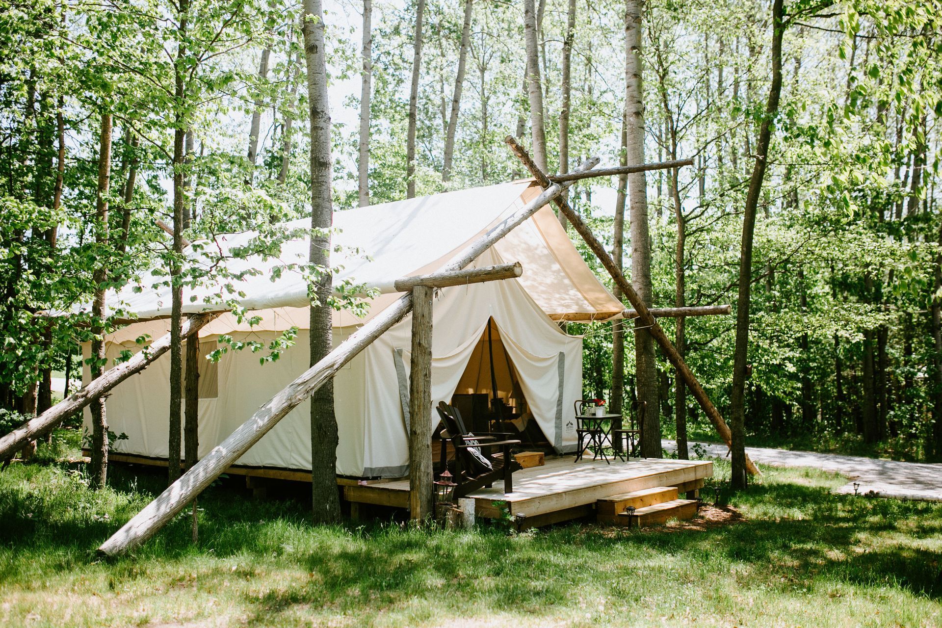 Canvas tent on a wooden deck in a forest setting. White and tan colors. Wooden supports.