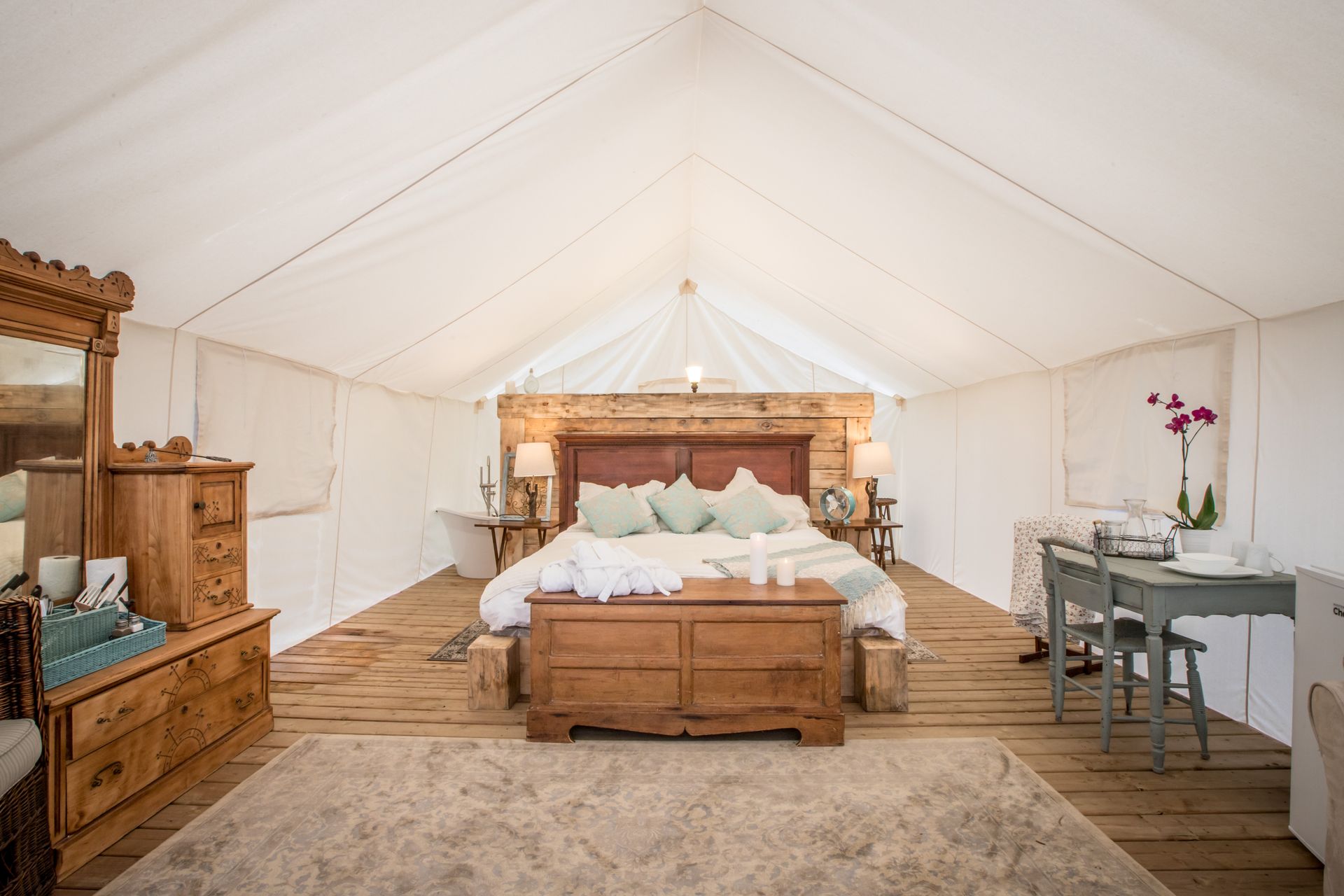 Spacious glamping tent interior with a large bed, wooden furniture, and a rug.