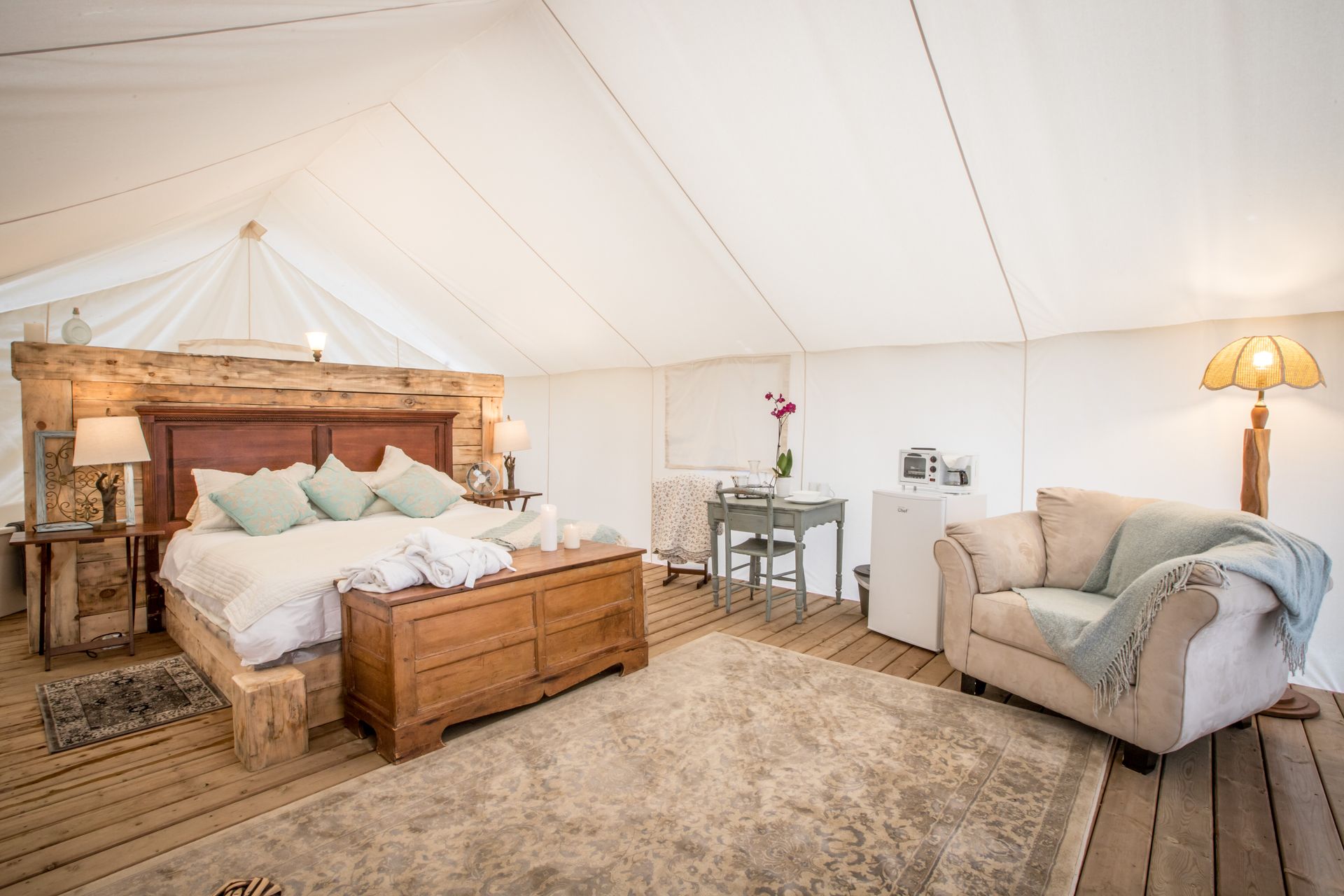 Spacious canvas tent interior with wooden bed, furniture, and seating.