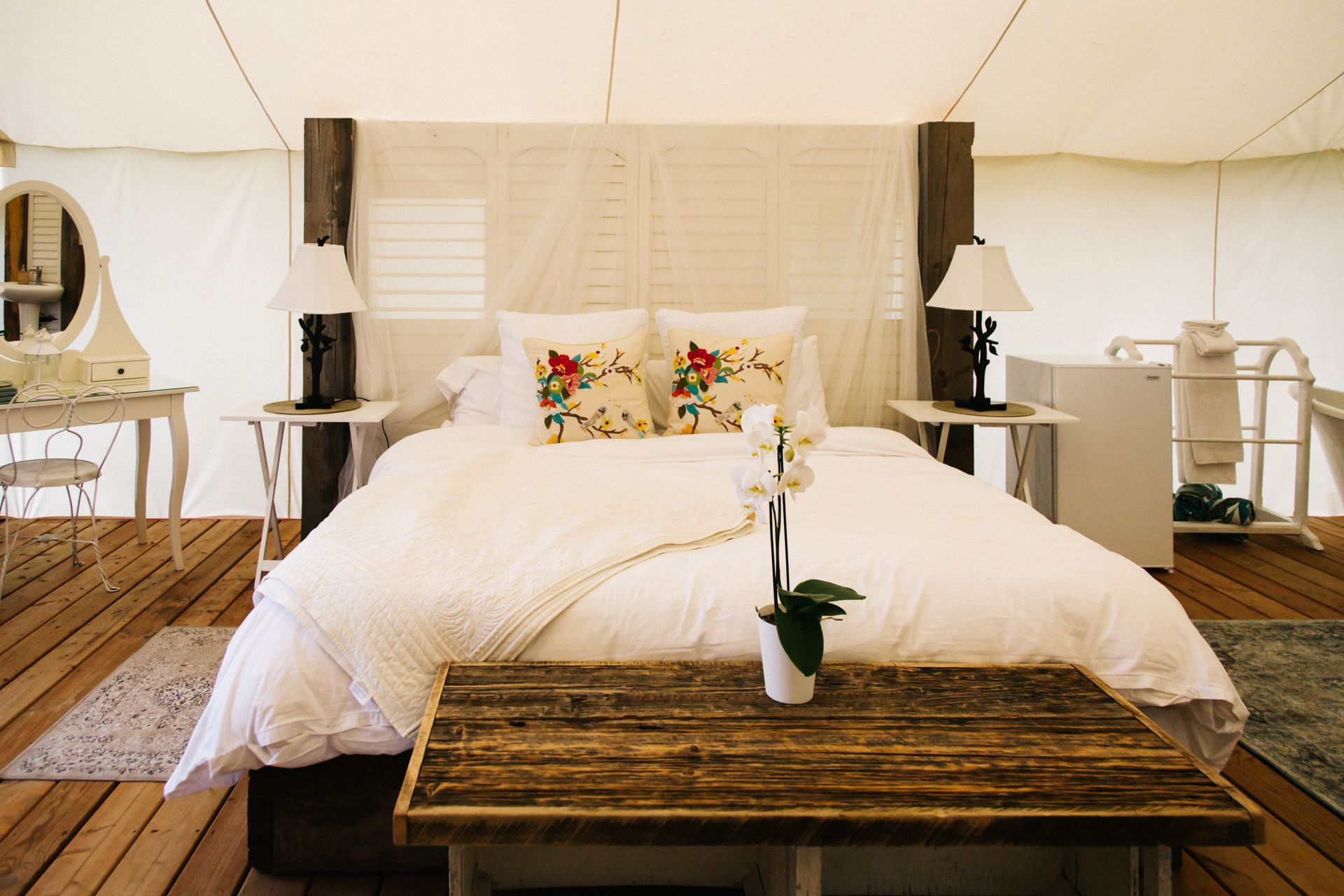 Bedroom interior of a tent with a bed, small tables, and a vanity.