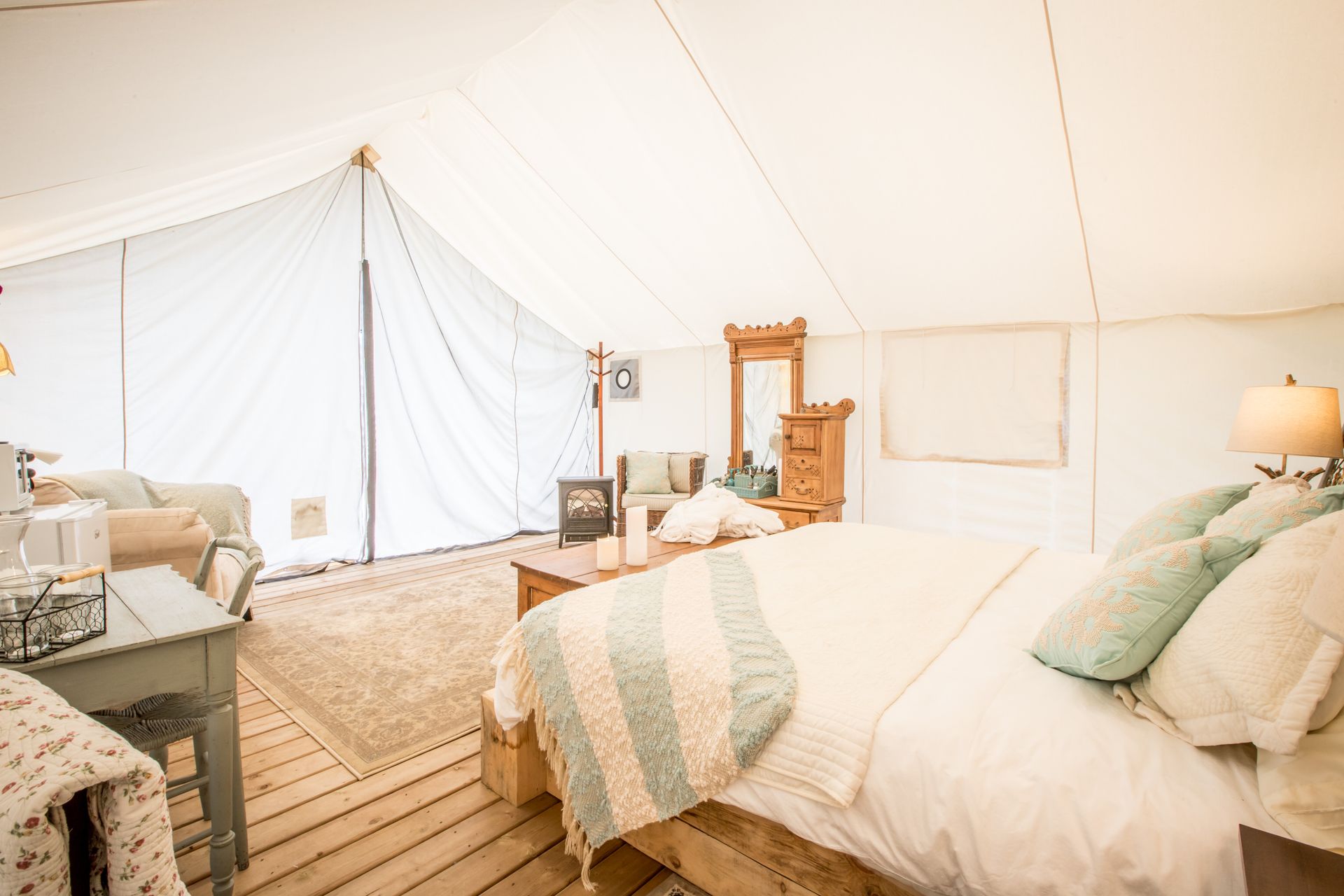 Inside of a luxury tent: bed, couch, fireplace, dresser, and lamps.