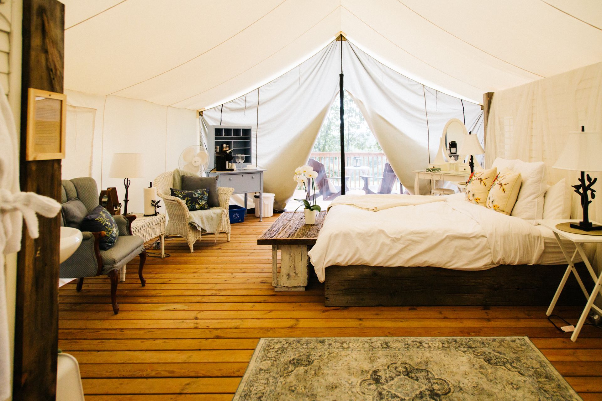 Interior of a glamping tent with bed, chairs, wood floor, and open window.