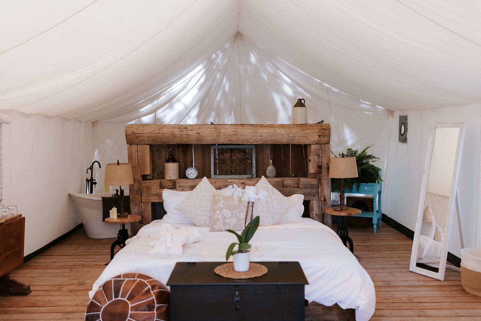 Bedroom inside a canvas tent, featuring a large bed with decorative headboard and mirror.