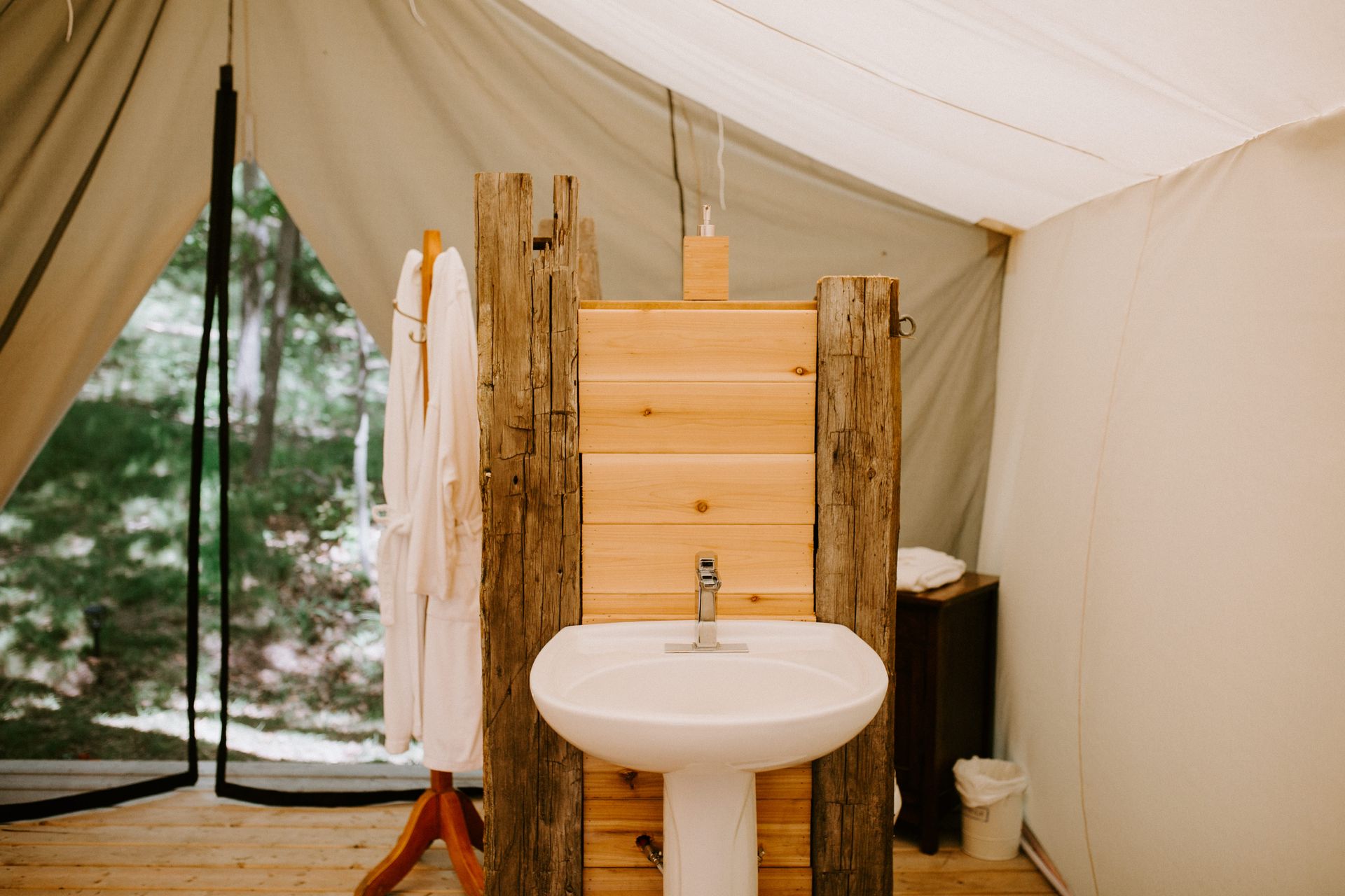 A rustic bathroom sink and shower inside a canvas tent, with a robe hanging nearby.