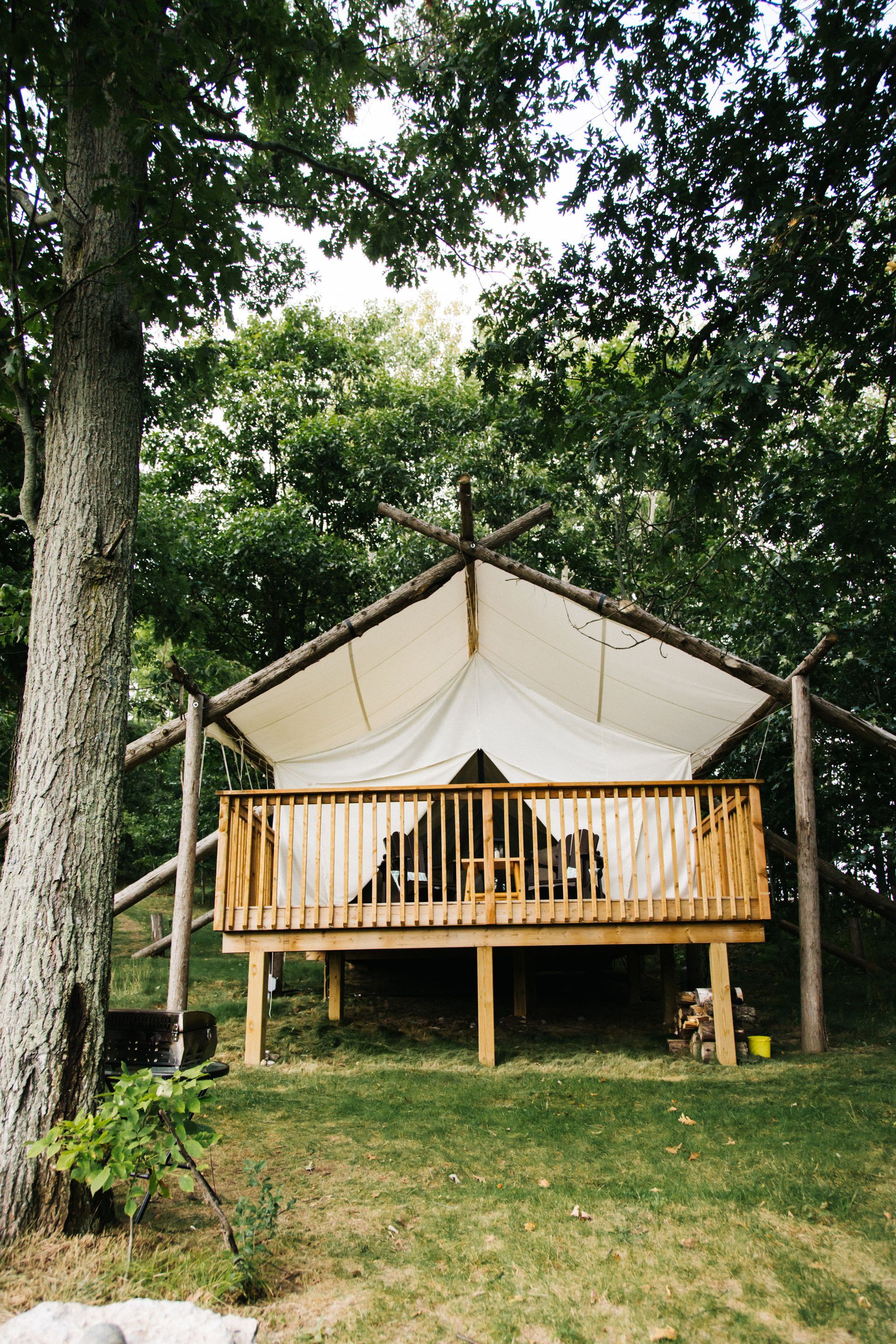 Wooden deck tent with a canvas roof, set in a wooded area.