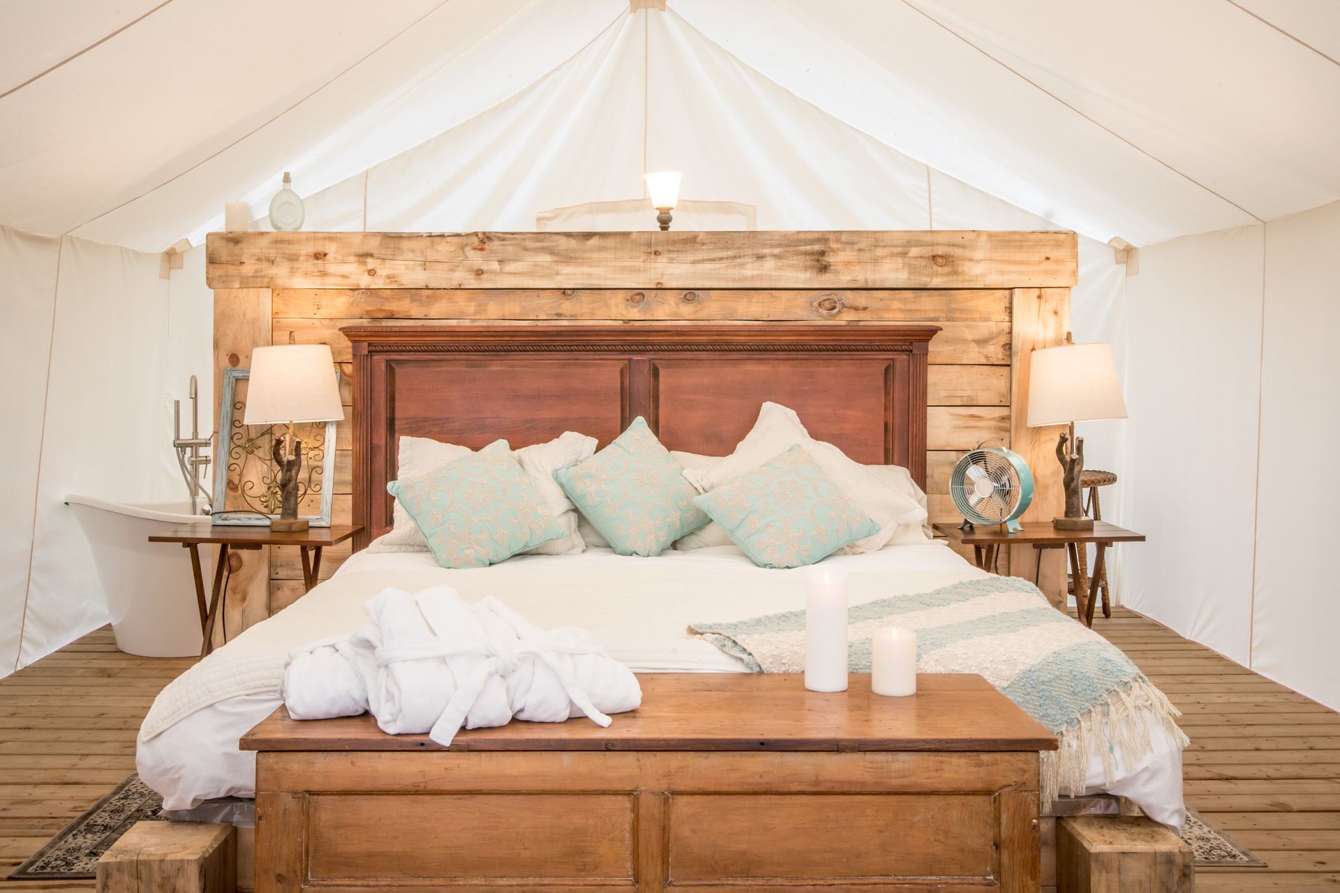 Cozy glamping tent interior with large bed, wooden furniture, and soft lighting.