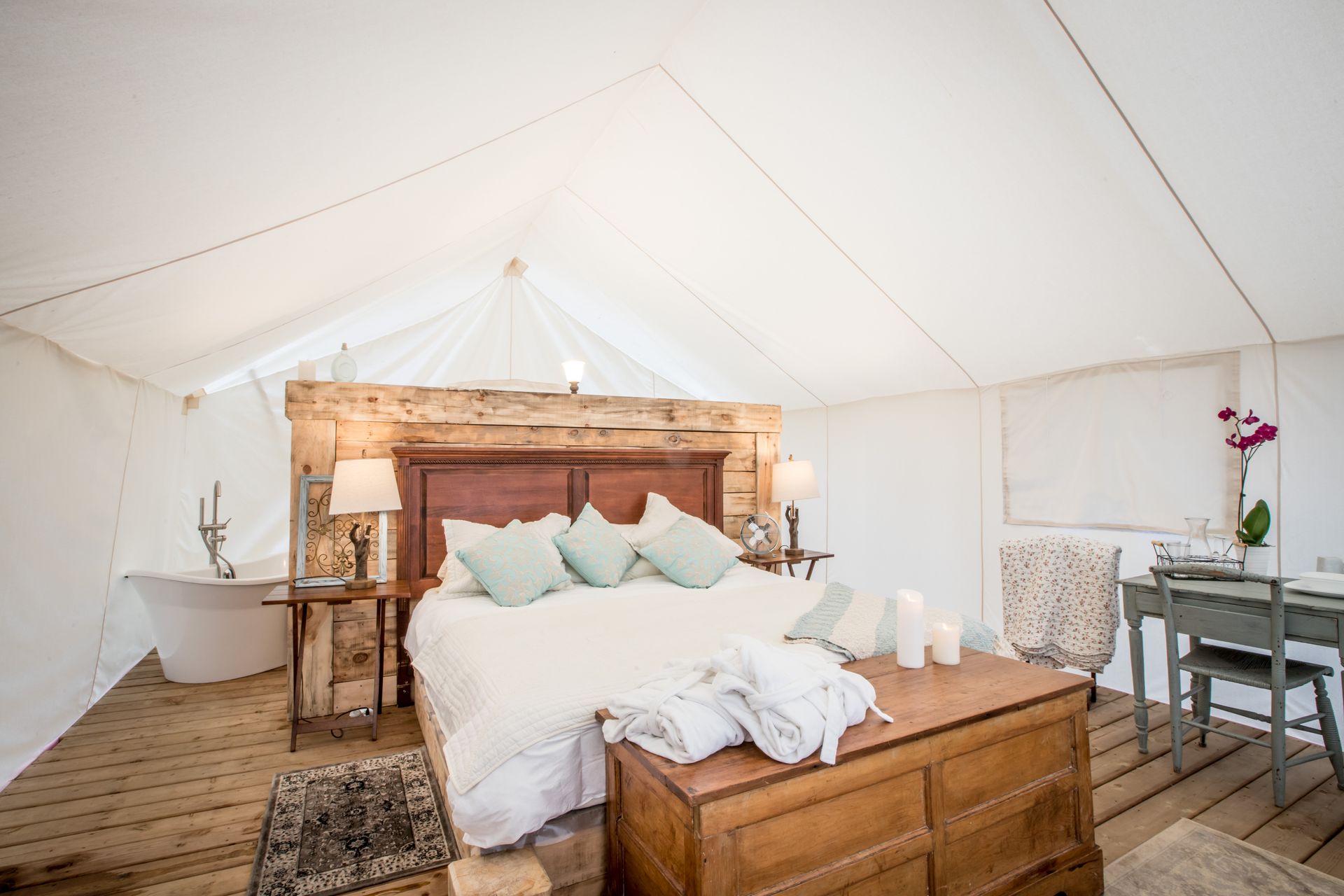 Spacious tent interior with a bed, wood accents, and a bathtub.
