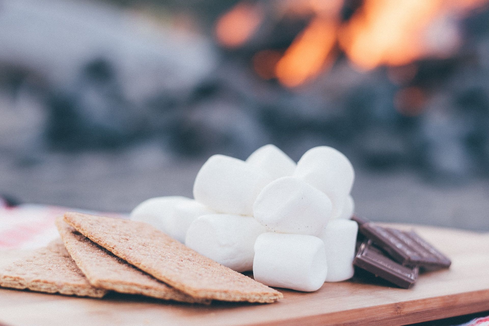 Graham crackers, marshmallows, and chocolate for s'mores, with a campfire in the background.