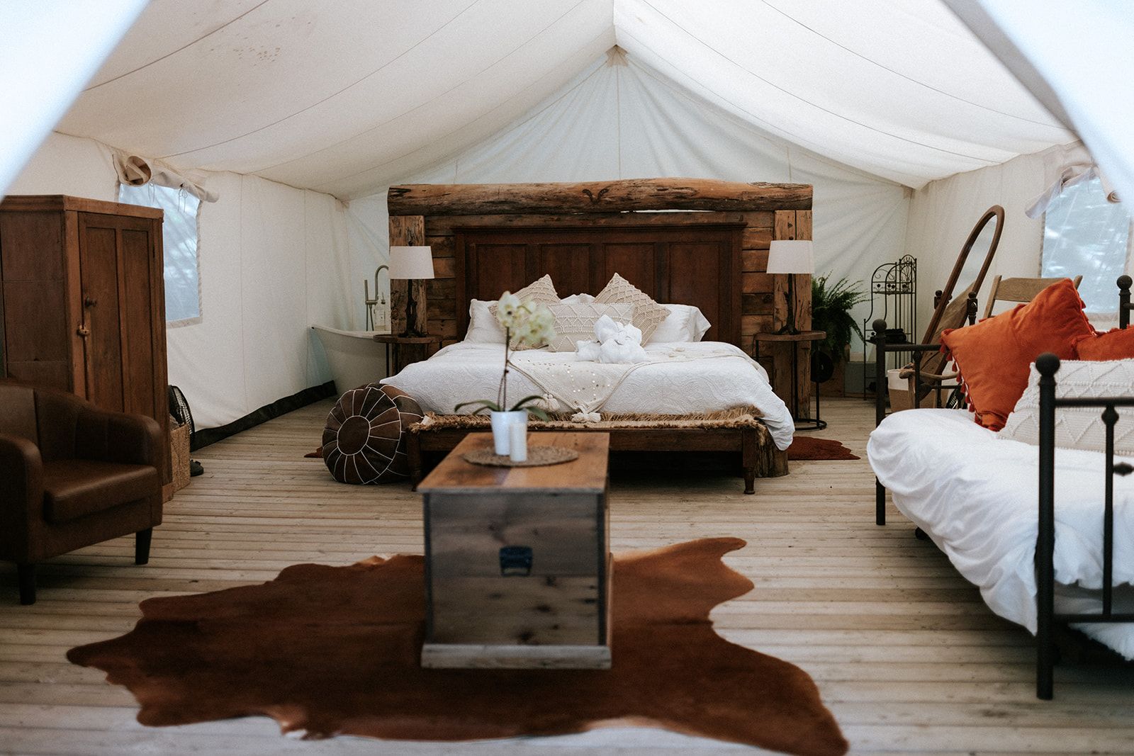 Spacious canvas tent interior with a large bed, seating, and wooden furniture on a wood floor, rustic decor.
