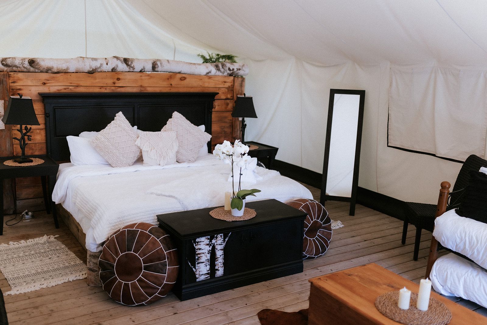 Bedroom inside a tent, featuring a large bed with pillows, a full-length mirror, and decorative furniture.