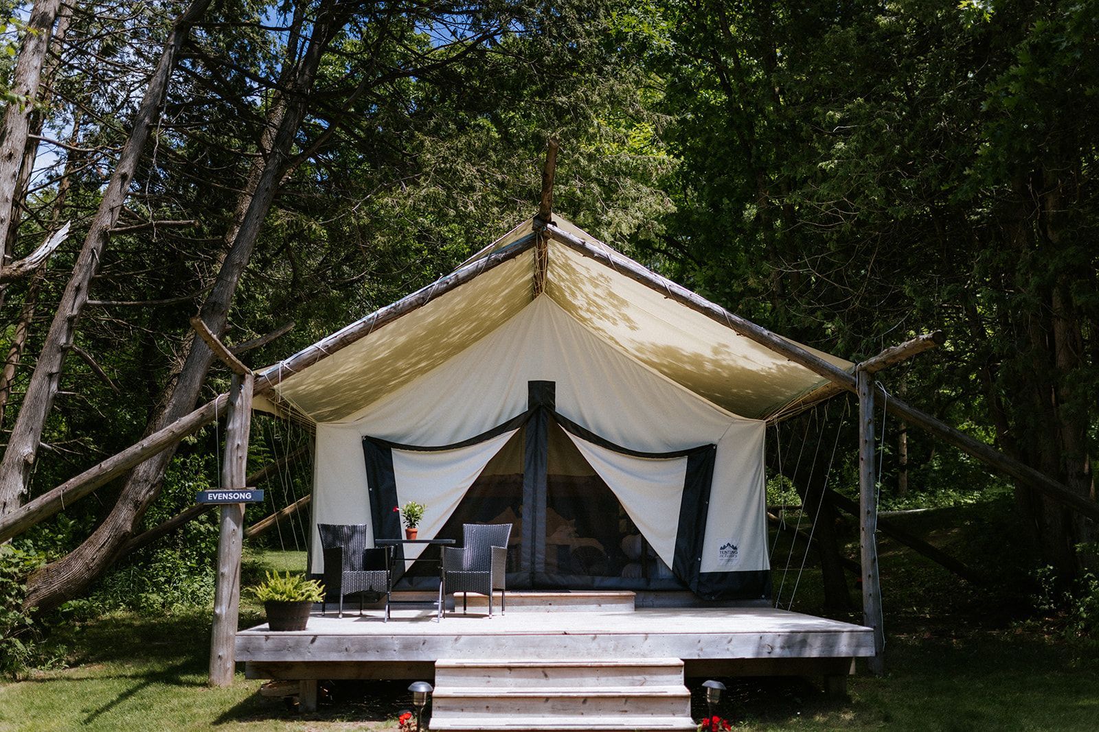 Canvas tent with wood frame and deck, two chairs, and table on a grassy setting.