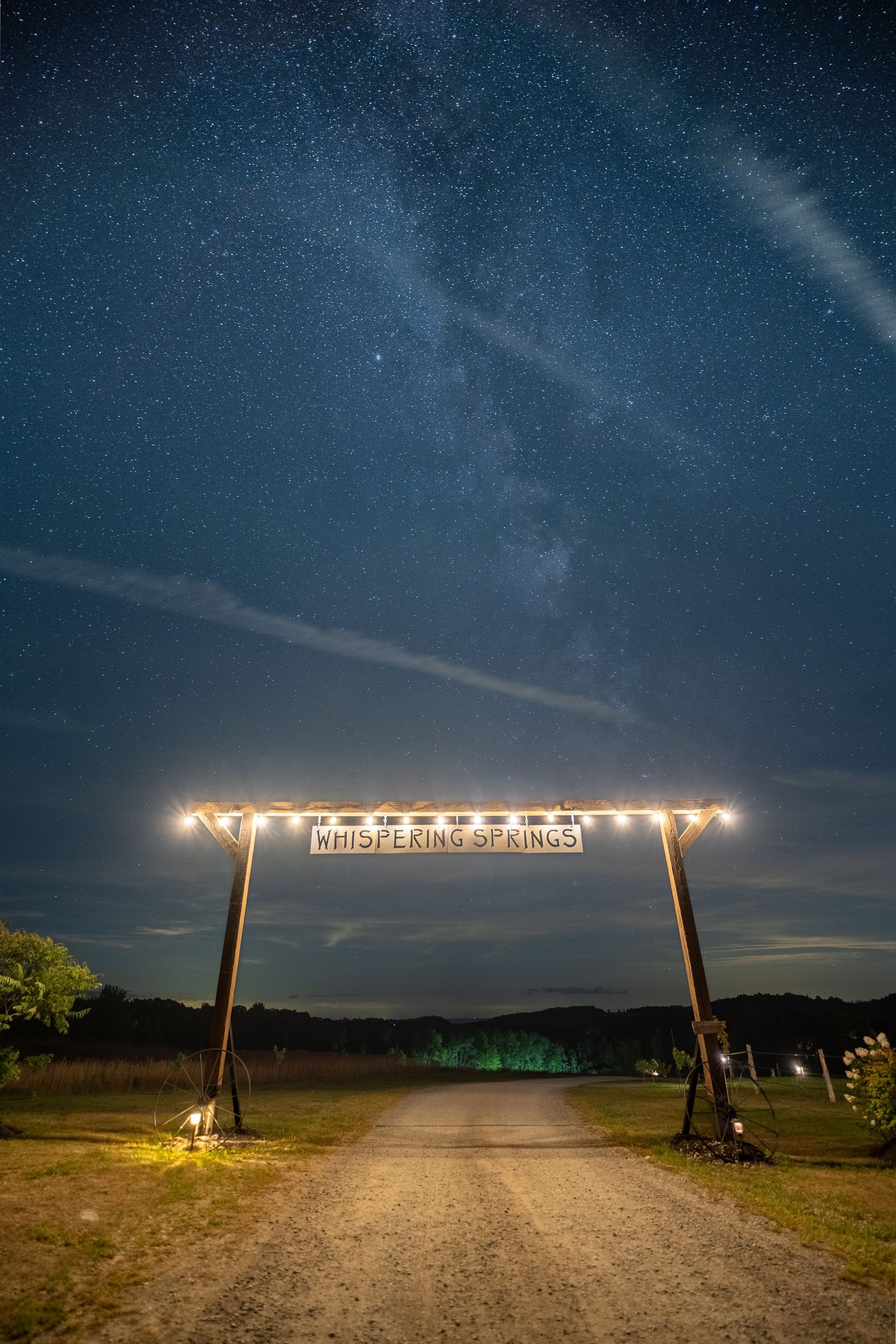Night sky over a lit archway with a gravel road leading to it. Milky Way visible.