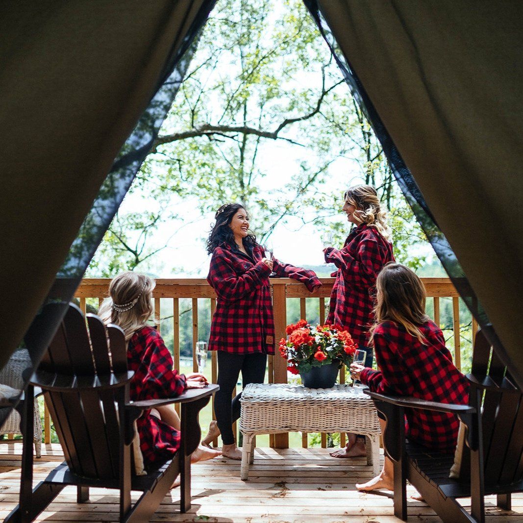 Four women in matching plaid shirts on a wooden deck, gathered around a small table with flowers.