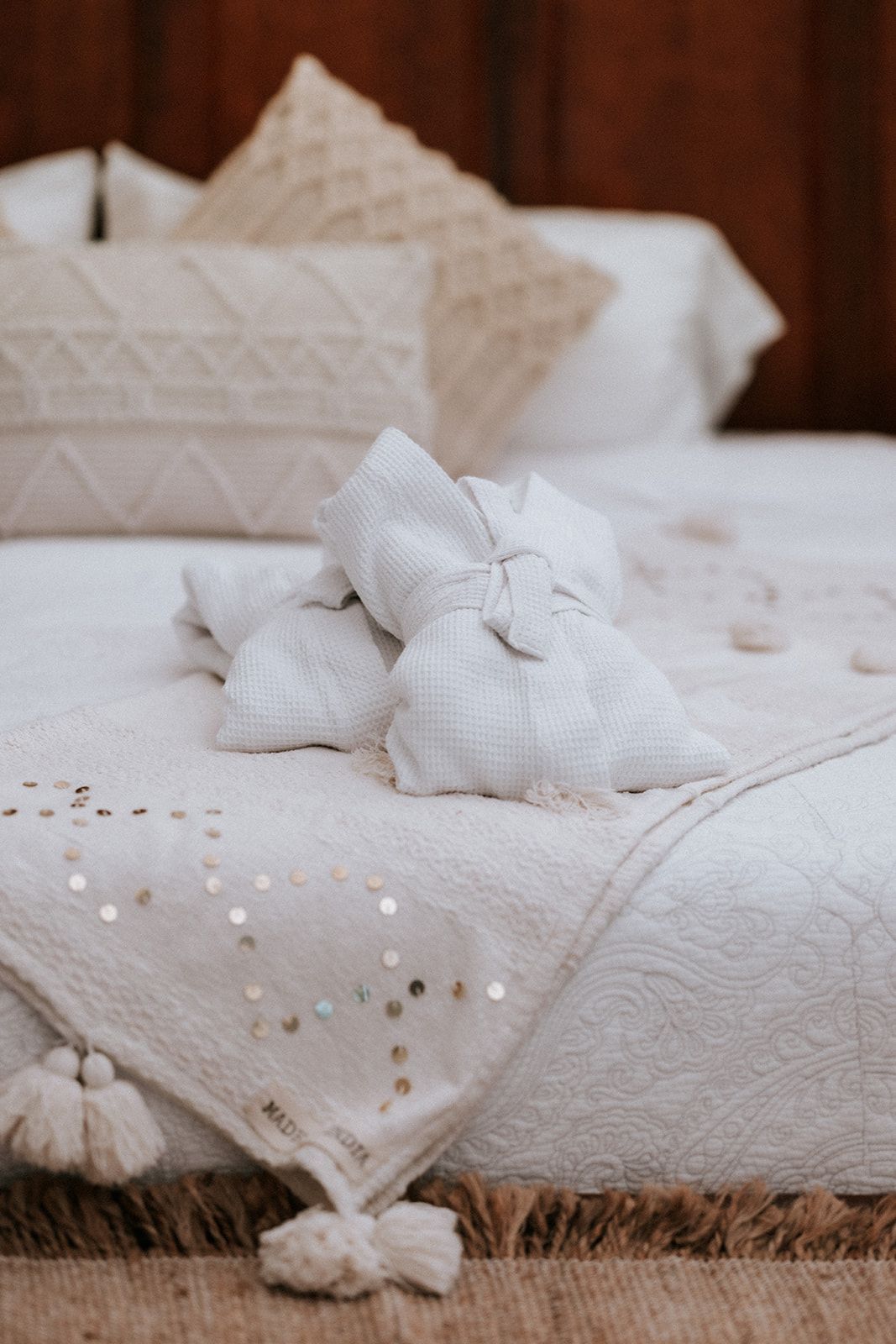 Bed with white linens, decorative pillows, folded towels, and a sequined throw.