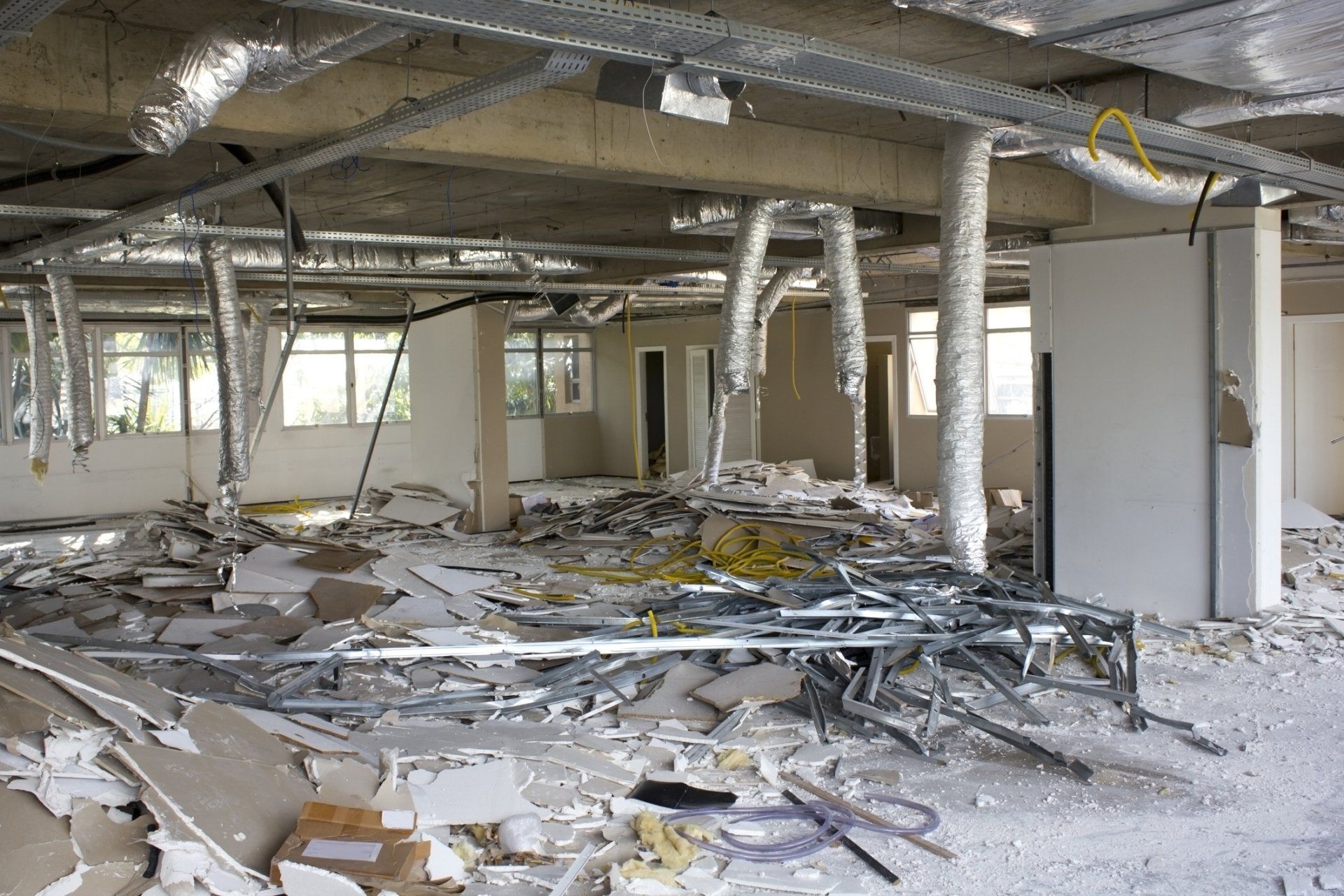 Debris-filled interior after demolition: scattered drywall, metal framing, exposed pipes and ductwork.