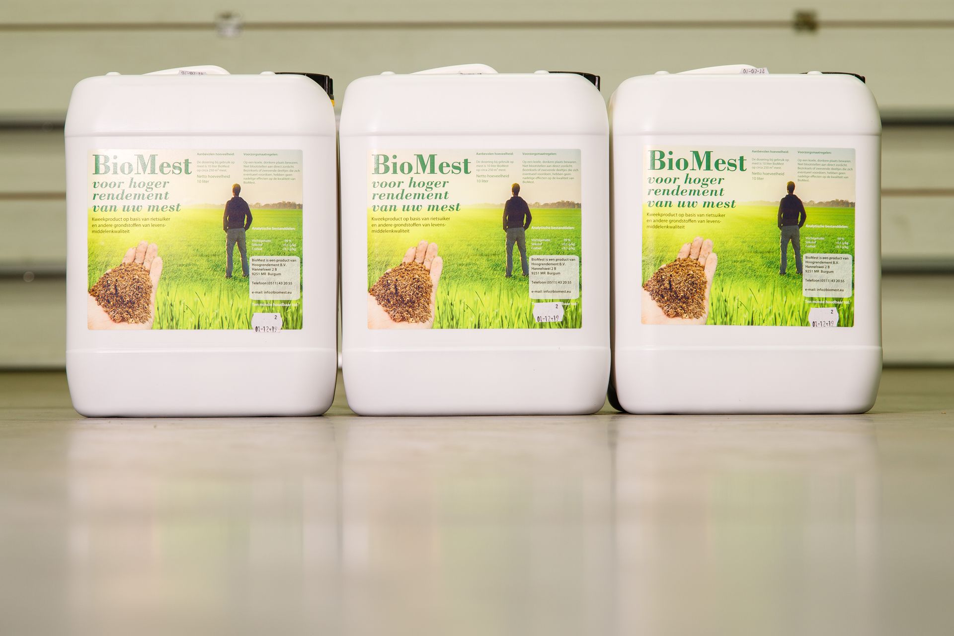 Drie witte BioMest-containers met groene etiketten staan in een loods.