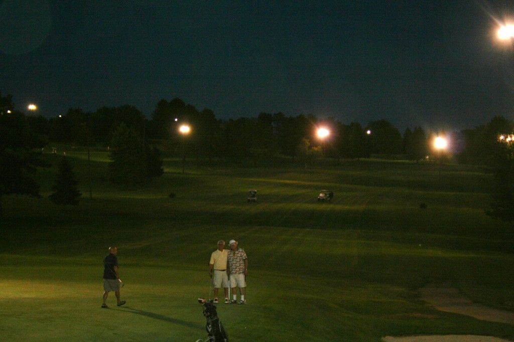 A couple of people standing on a golf course at night