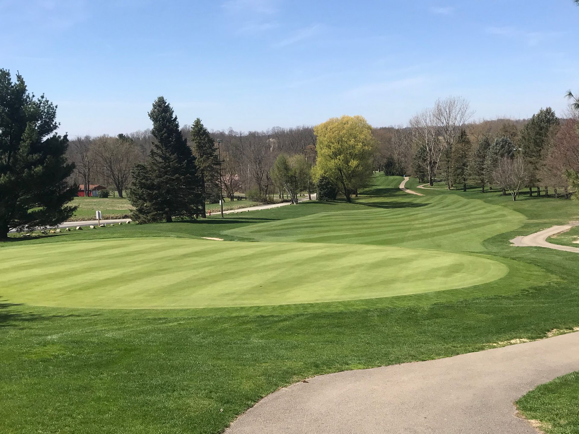A golf course with a path leading to the green and trees in the background.