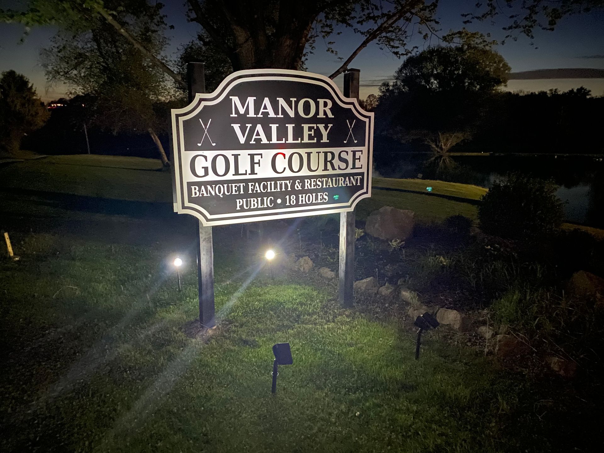A manor valley golf course sign is lit up at night