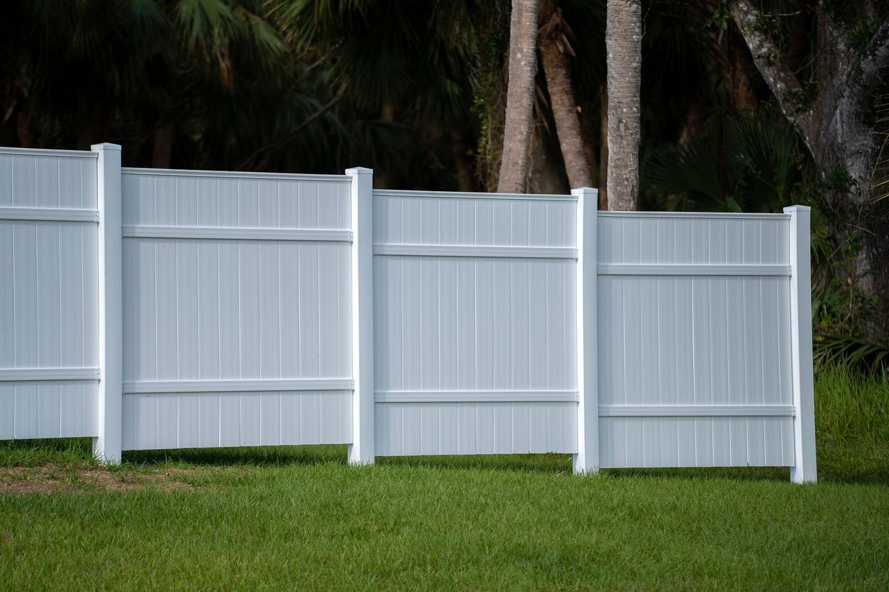 A white vinyl fence is sitting in the middle of a lush green field.