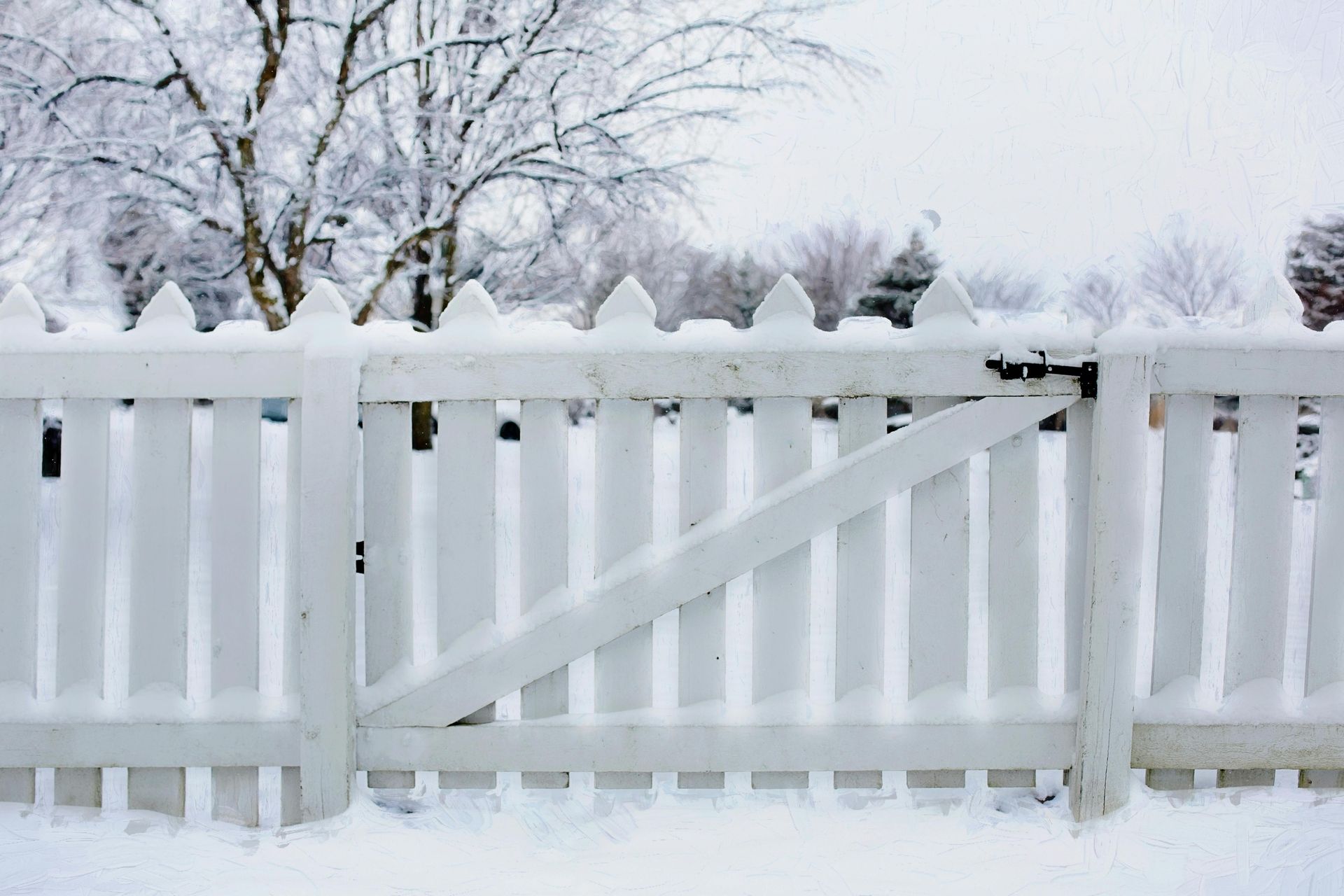 A white picket fence covered in snow with trees in the background.