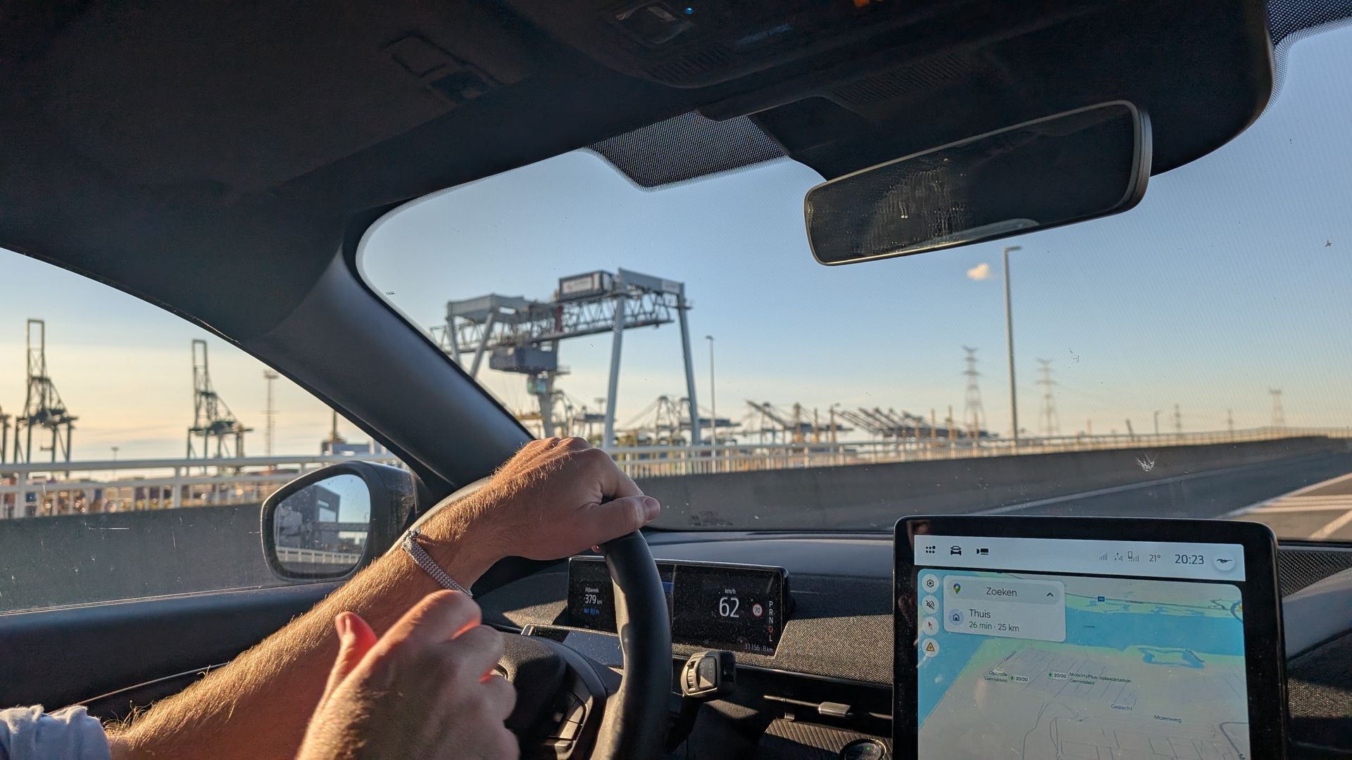 Man rijdt in een auto met een tablet waarop een kaart te zien is. In de verte zijn havenkranen te zien.