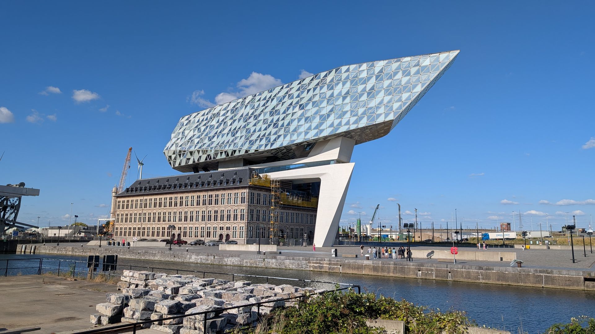 Modern wit kantoorpand van glas bovenop een ouder bakstenen gebouw aan een waterweg in Antwerpen, België.