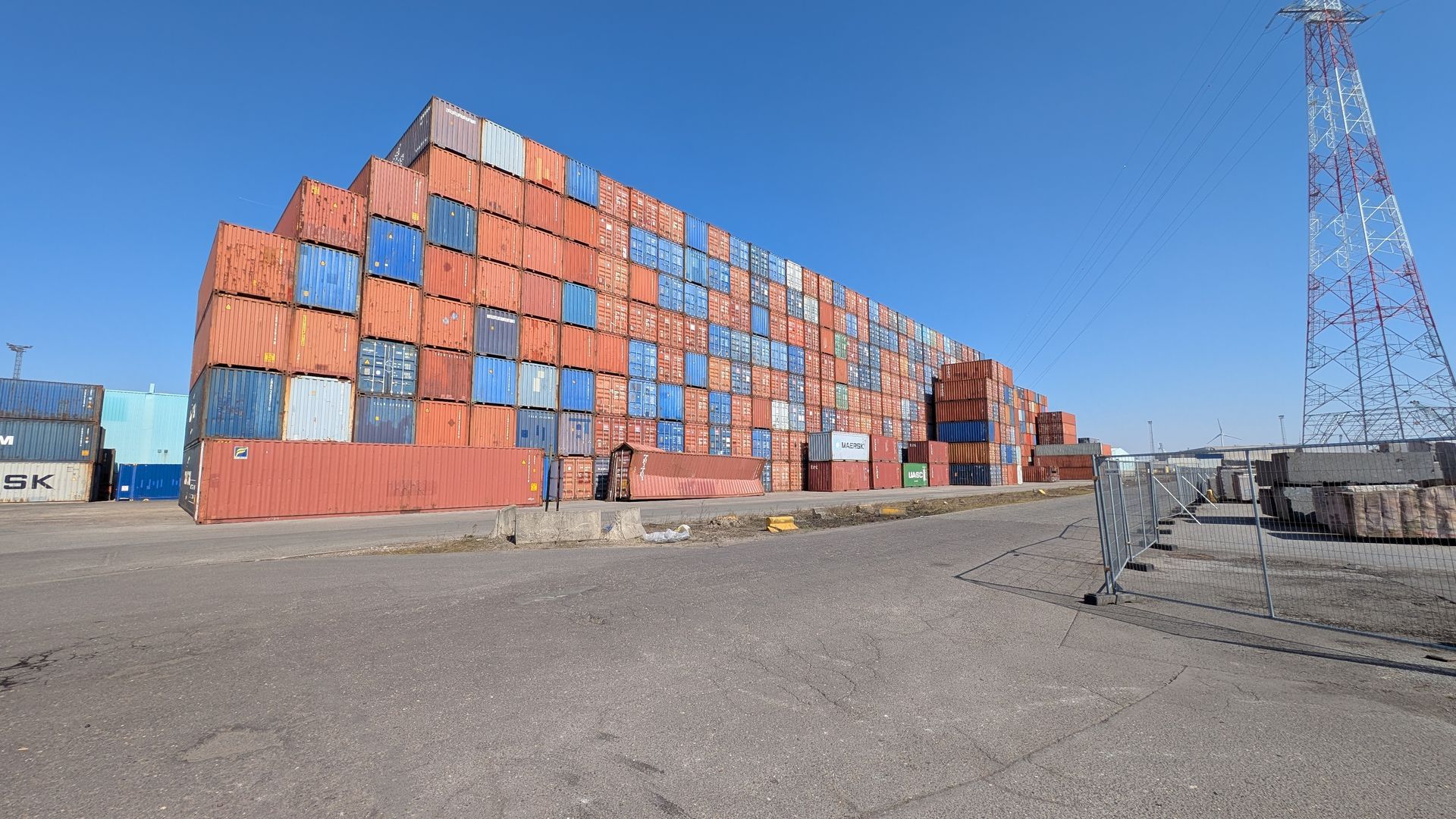 Vrachtcontainers opgestapeld op een groot buitenterrein, met de blauwe lucht op de achtergrond.