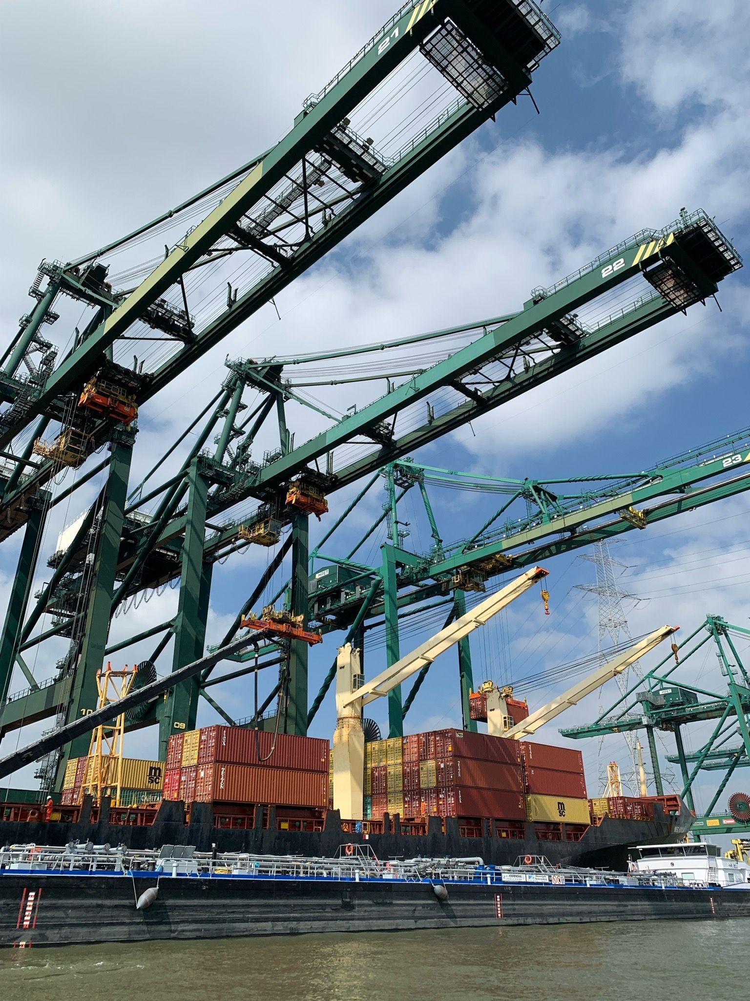 Grues de transport dominant un cargo et des barges dans un port, ciel bleu avec des nuages.