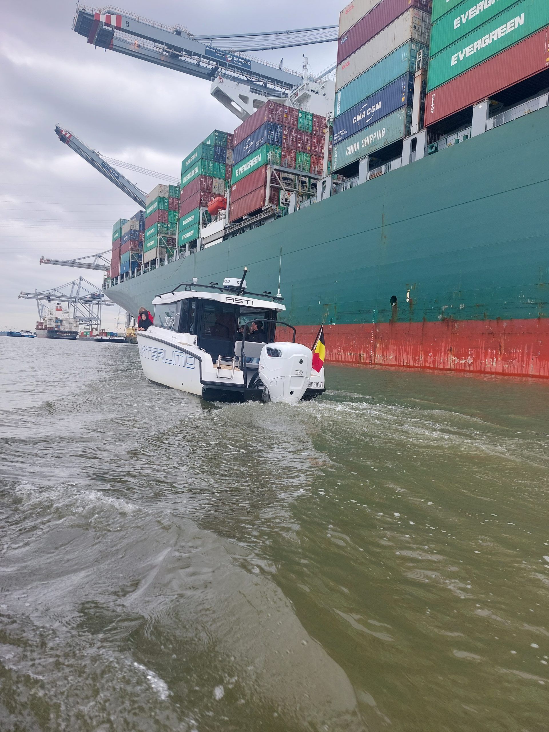 Un bateau blanc navigue sur l'eau près d'un cargo vert géant dans un port.