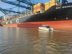 Small white boat on water in front of a large black and red cargo ship, MSC Madrid.