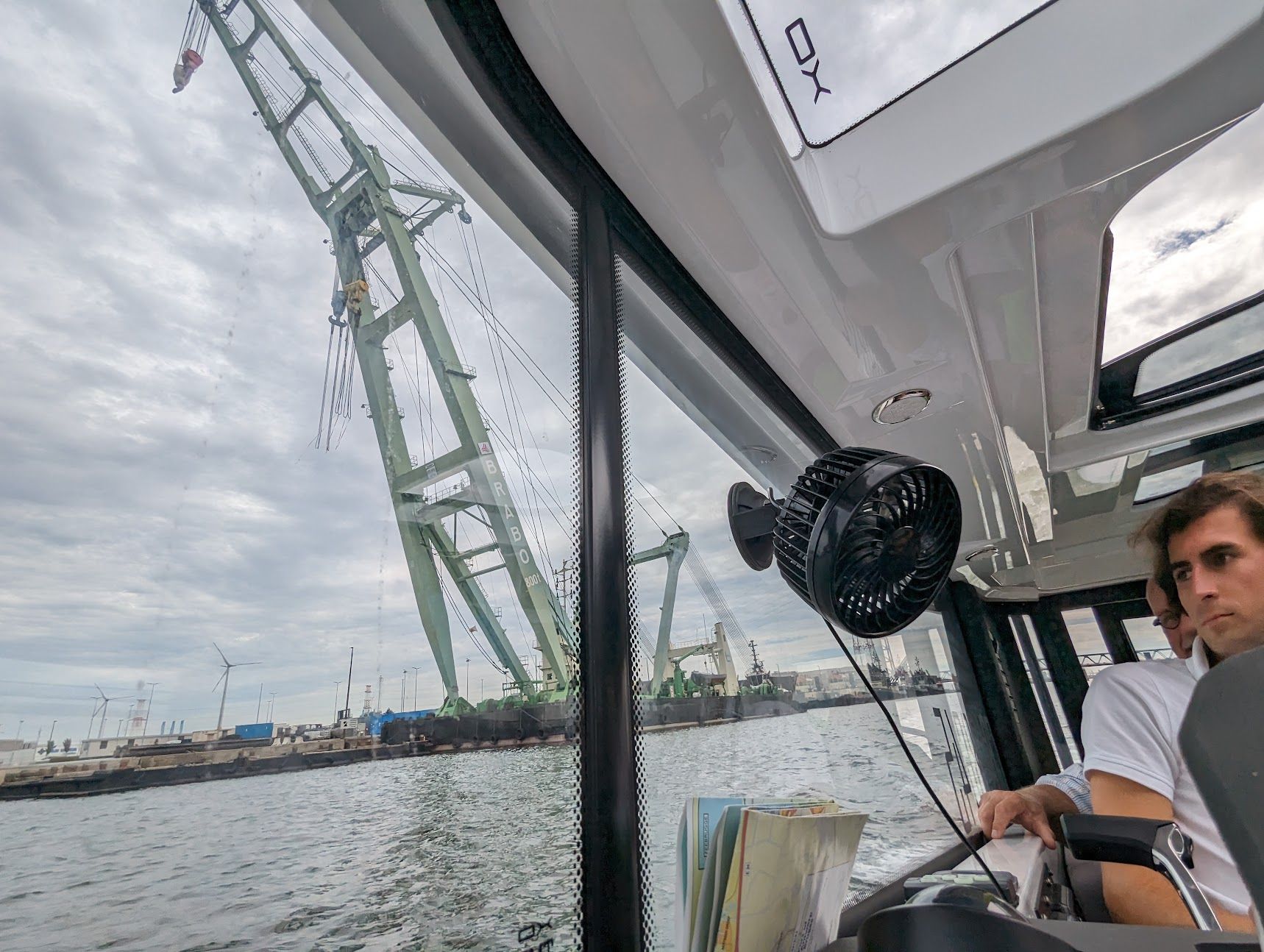 Une personne dirige un bateau près d'une grande grue industrielle par temps nuageux.