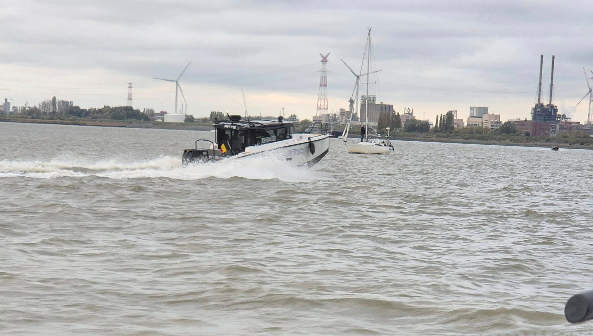 Un bateau noir filant à toute vitesse sur des eaux agitées, un arrière-plan industriel