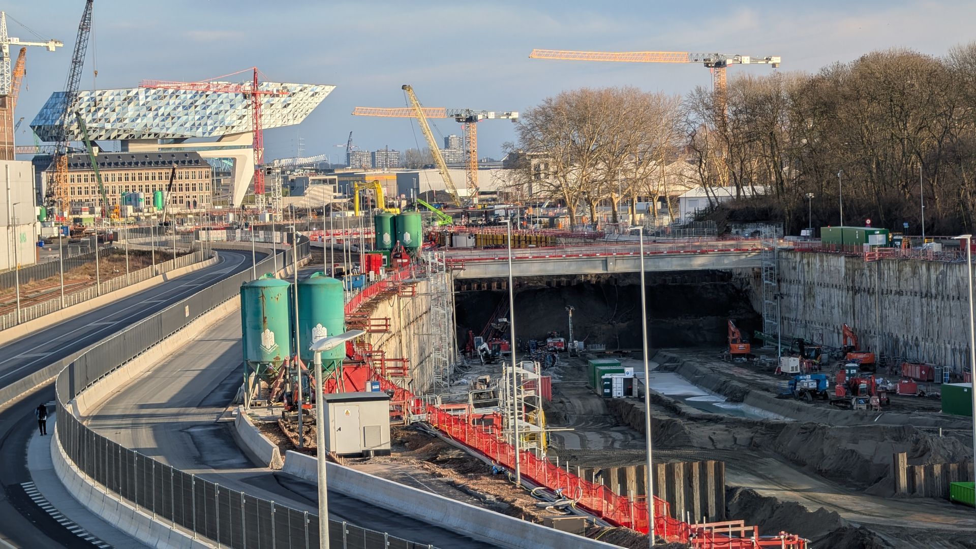 Man taking selfie with group of people on scooters in front of cargo ship at dock.