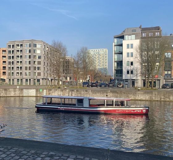 Man taking selfie with group of people on scooters in front of cargo ship at dock.