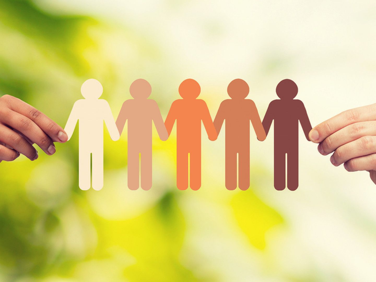 Hands holding diverse paper cut-out figures representing unity and inclusion against a green backdrop.