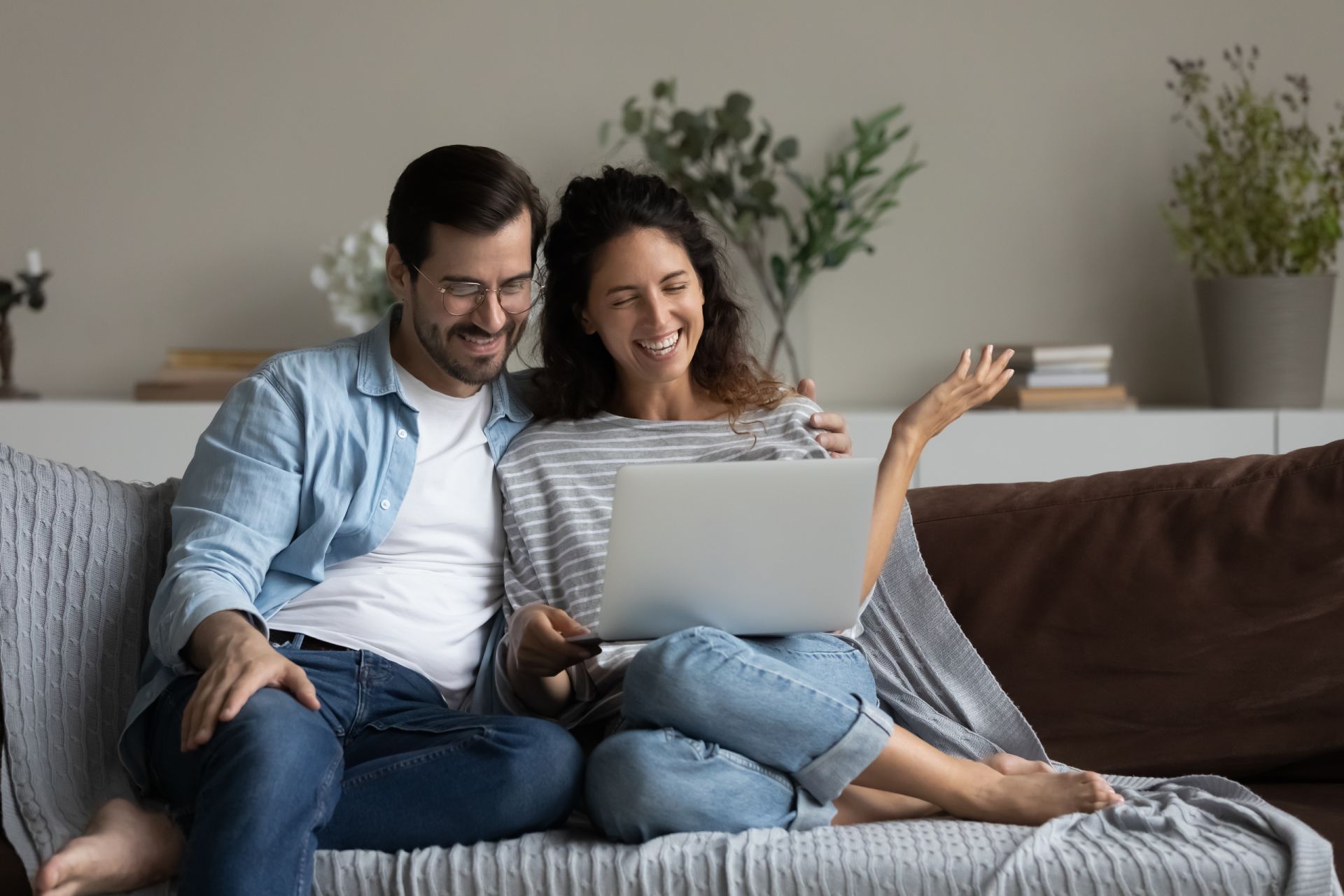 Couple on couch, smiling at laptop screen, arm around each other.