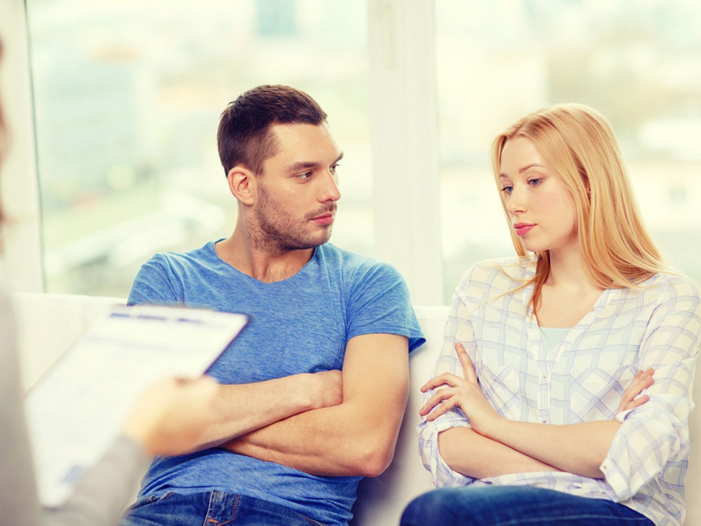 A couple with arms crossed looking concerned, sitting during a therapy session.