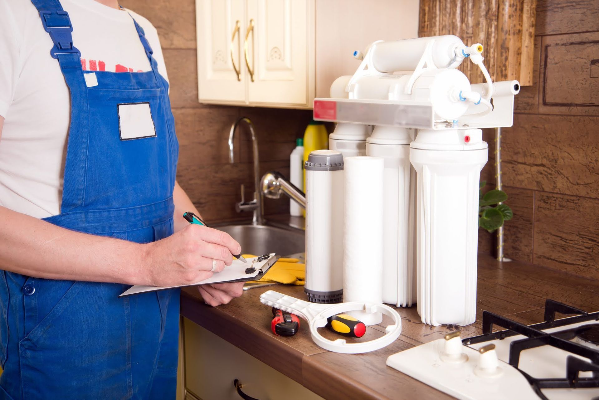 A plumber is working on a water filter in a kitchen.