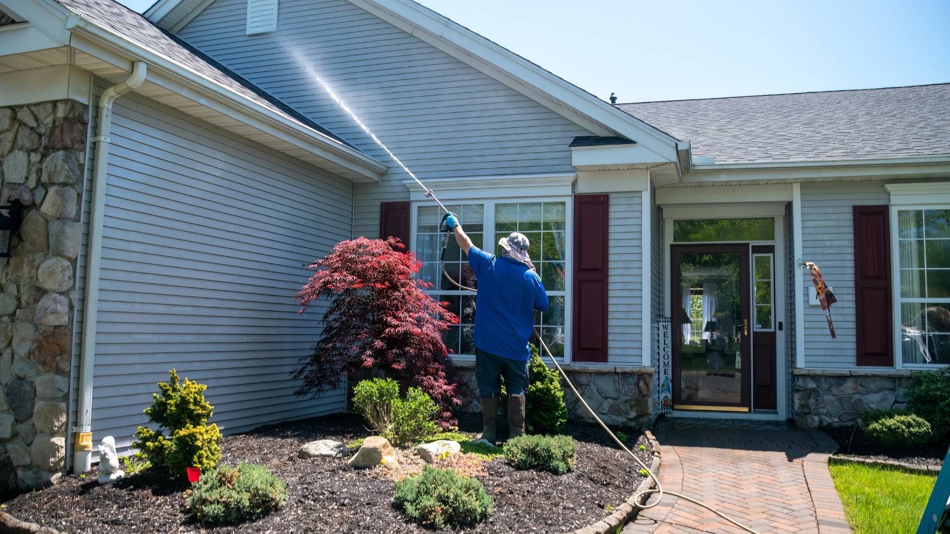 A man is cleaning the side of a house with a pressure washer.