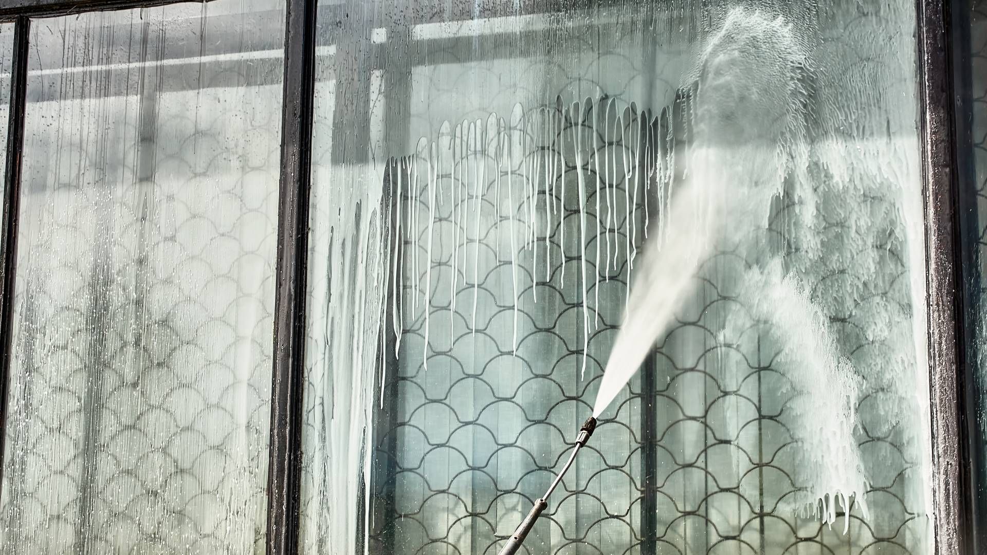 A person is cleaning a window with a high pressure washer.