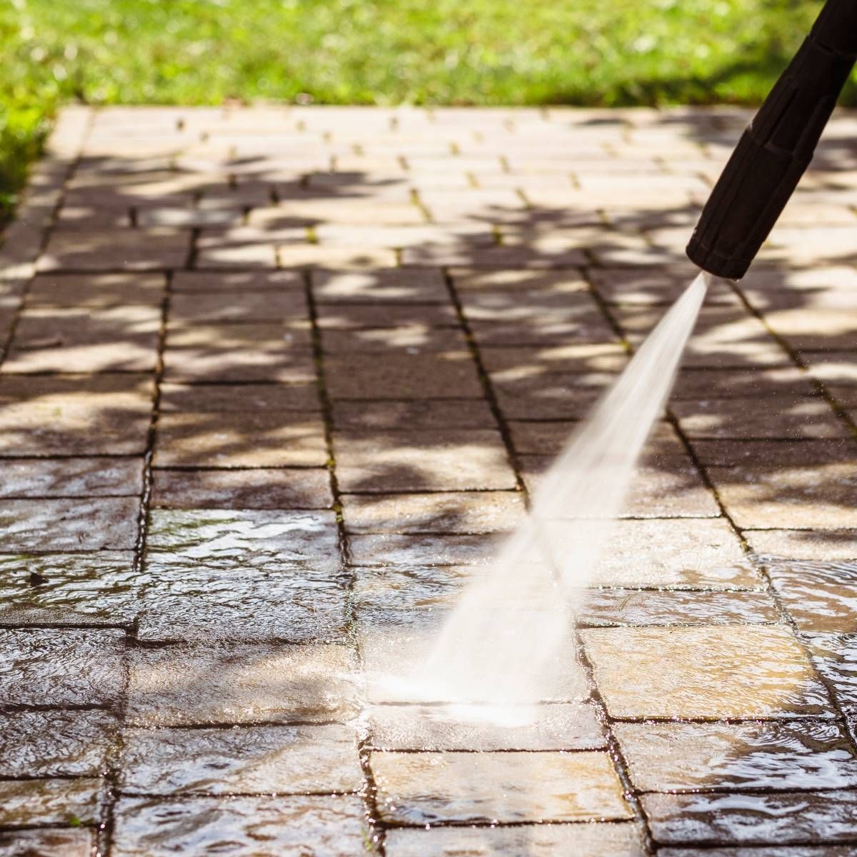 A person is using a high pressure washer to clean a brick walkway.